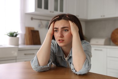 Photo of Scared woman suffering from paranoia at table in kitchen