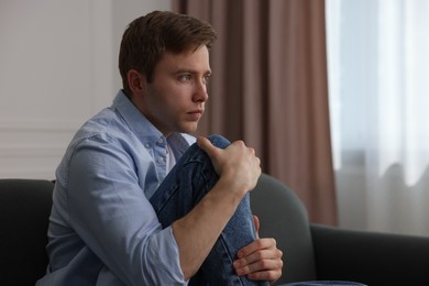 Photo of Man suffering from paranoia on sofa at home, space for text