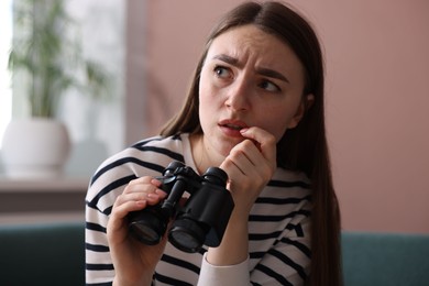 Photo of Paranoia. Worried man with binoculars at home