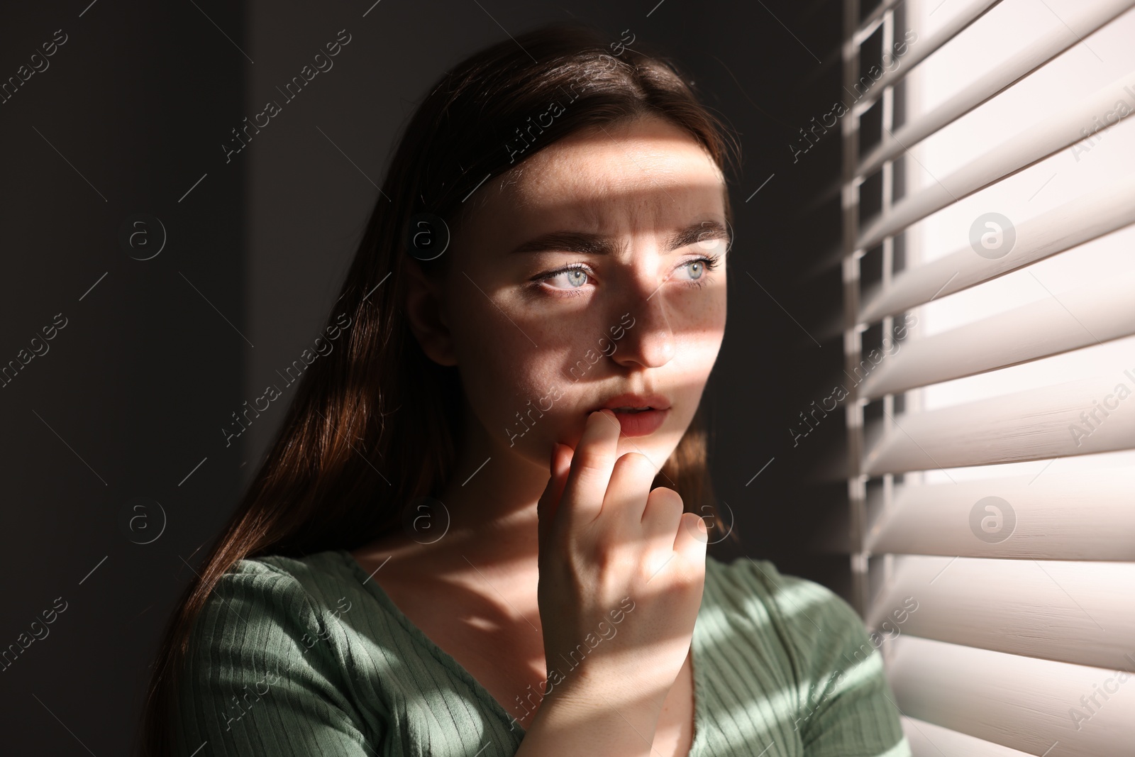 Photo of Paranoia. Worried woman near window at home