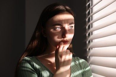 Photo of Paranoia. Worried woman near window at home