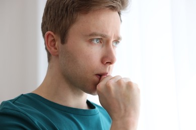 Photo of Paranoia. Worried man near window at home, space for text