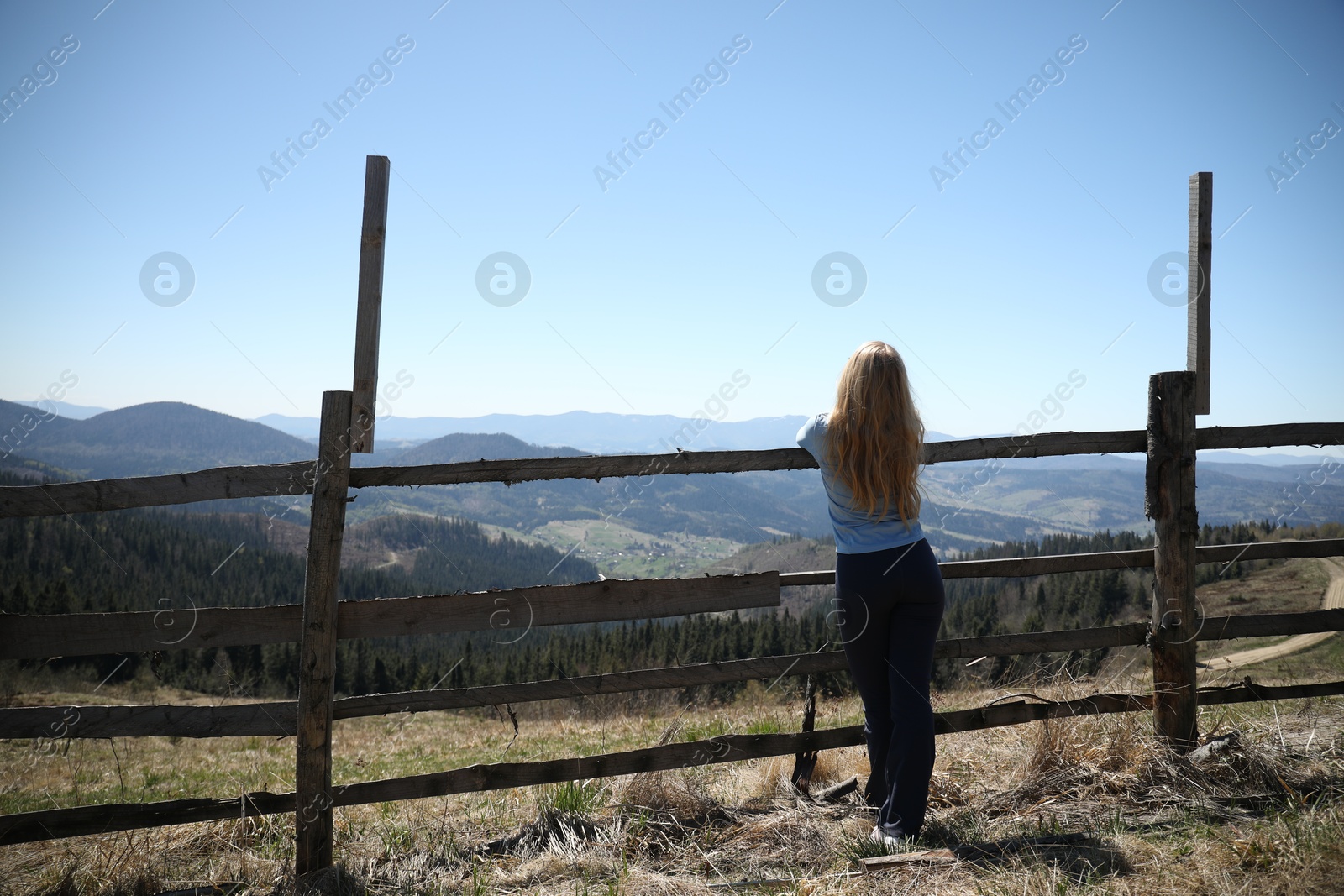 Woman near wooden fence in mountains, back view Photo of Woman near wooden fence in mountains, back view