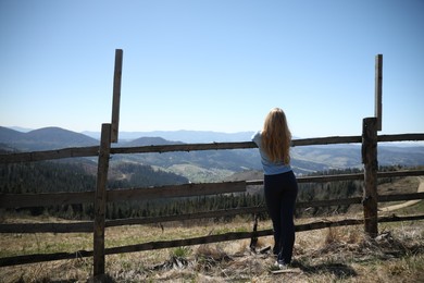 Photo of Woman near wooden fence in mountains, back view