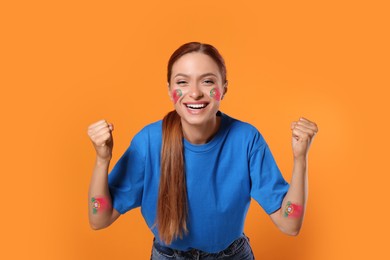 Image of Excited fan with flags of Portugal painted on her face and arms against orange background