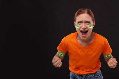 Image of Excited fan with flags of Brazil painted on her arms against black background. Space for text