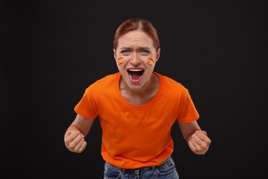 Image of Excited fan with flags of Spain painted on her face against black background