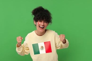 Image of Excited fan with flag of Mexico on her sweater against green background