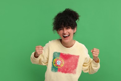 Image of Excited fan with flag of Portugal on her sweater against green background