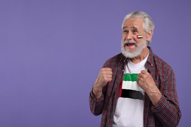 Image of Excited fan with flags of United Arab Emirates on his face and t-shirt against dark violet background. Space for text