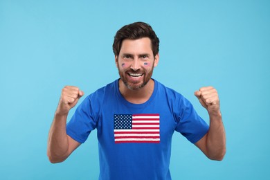 Image of Excited fan with flags of USA on his face and t-shirt against light blue background
