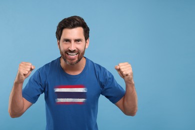 Image of Excited fan with flag of Thailand on his t-shirt against light blue background. Space for text