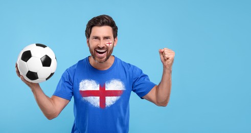 Image of Excited fan with flags of England on his face and t-shirt holding soccer ball against light blue background. Banner design with space for text