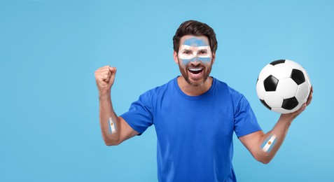 Image of Excited fan with flags of Argentina painted on his arms holding soccer ball against light blue background. Banner design with space for text
