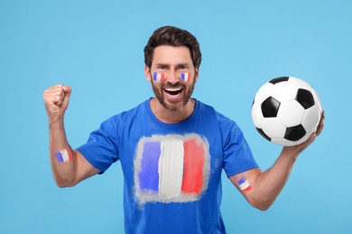 Image of Excited fan with flags of France on his body and t-shirt holding soccer ball against light blue background