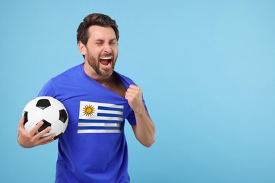 Image of Excited fan with flag of Uruguay on his t-shirt holding soccer ball against light blue background. Space for text