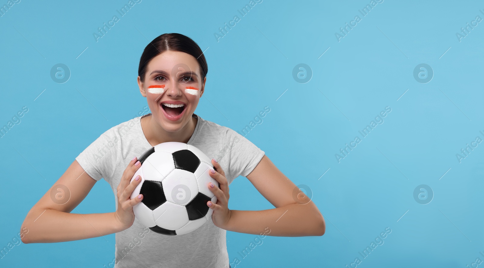 Excited fan with flags of Monaco painted on her face holding soccer ball against light blue background. Banner design with space for text Image of Excited fan with flags of Monaco painted on her face holding soccer ball against light blue background. Banner design with space for text