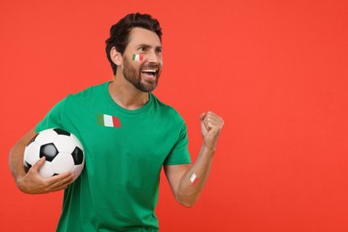 Image of Excited fan with flags of Italy on his body and t-shirt holding soccer ball against red background. Space for text
