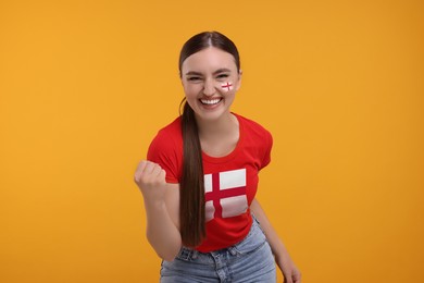 Image of Excited fan with flags of England on her face and t-shirt against orange background