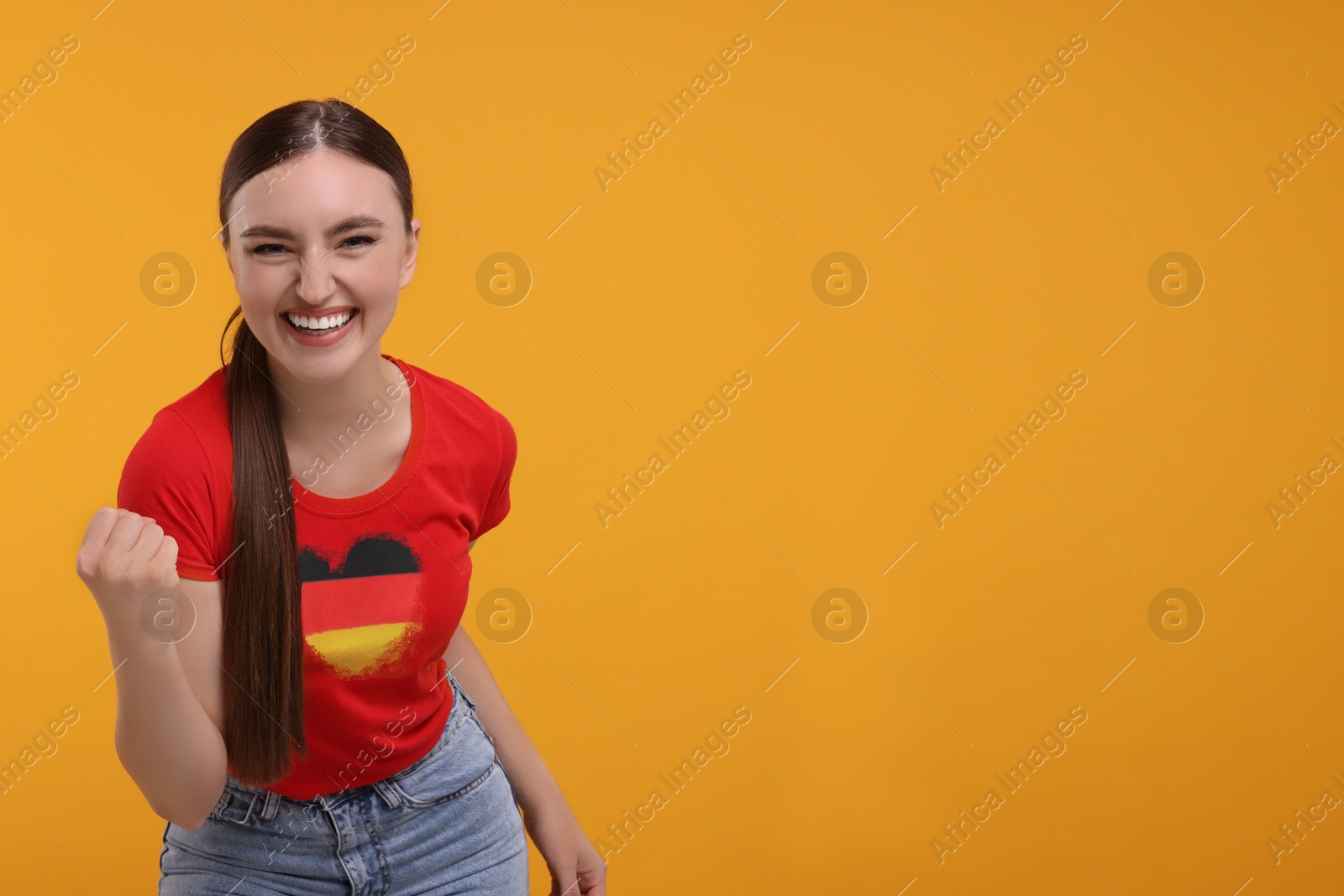 Excited fan with flag of Germany on her t-shirt against orange background. Space for text Image of Excited fan with flag of Germany on her t-shirt against orange background. Space for text