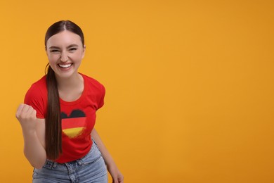 Image of Excited fan with flag of Germany on her t-shirt against orange background. Space for text