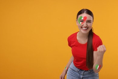 Image of Excited fan with flags of Italy painted on her body against orange background. Space for text
