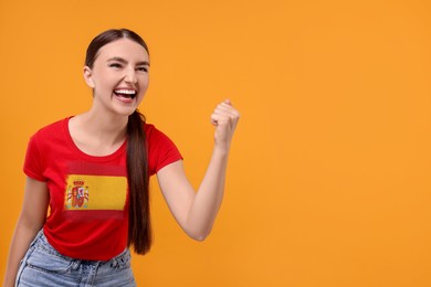 Image of Excited fan with flag of Spain on her t-shirt against orange background. Space for text
