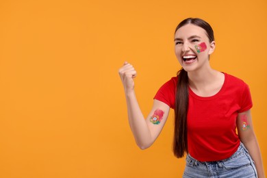 Image of Excited fan with flags of Portugal painted on her body against orange background. Space for text