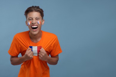 Image of Excited fan with flags of France on his face and t-shirt against light blue background. Space for text