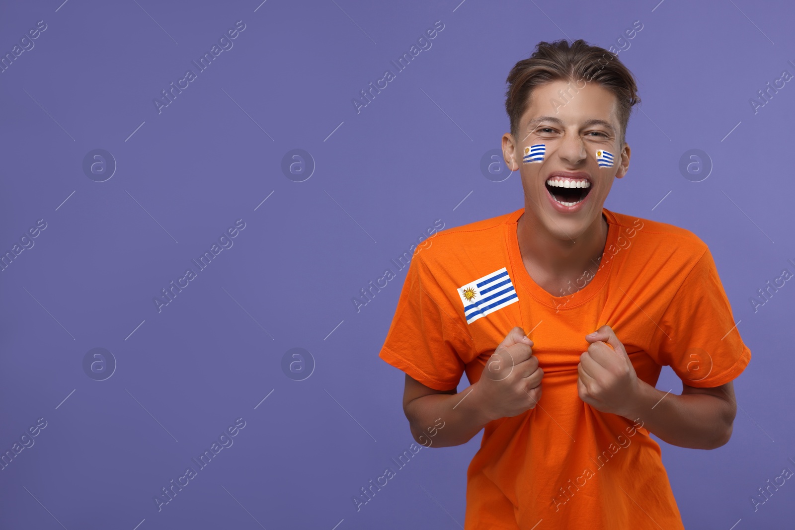 Excited fan with flags of Uruguay on his face and t-shirt against dark violet background. Space for text Image of Excited fan with flags of Uruguay on his face and t-shirt against dark violet background. Space for text