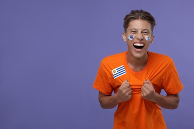Image of Excited fan with flags of Uruguay on his face and t-shirt against dark violet background. Space for text