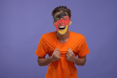 Image of Excited fan with flag of Germany painted on his face against dark violet background