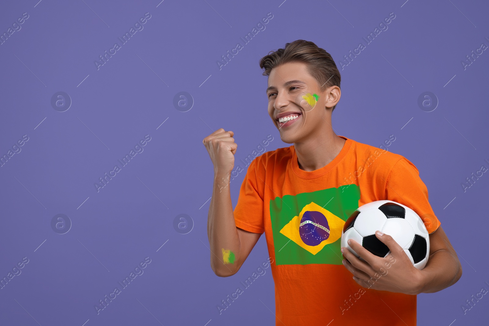 Excited fan with flag of Brazil on his t-shirt holding soccer ball against dark violet background. Space for text Image of Excited fan with flag of Brazil on his t-shirt holding soccer ball against dark violet background. Space for text
