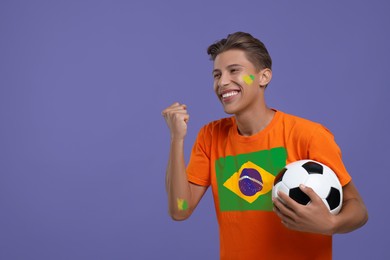 Image of Excited fan with flag of Brazil on his t-shirt holding soccer ball against dark violet background. Space for text