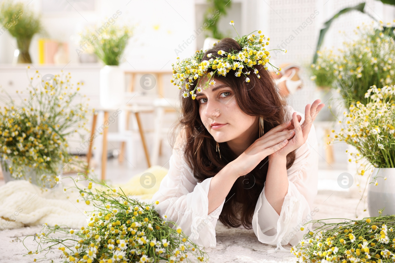 Beautiful woman with chamomile flowers on floor indoors Photo of Beautiful woman with chamomile flowers on floor indoors