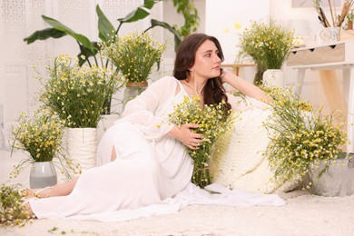 Photo of Beautiful woman with chamomile flowers on floor indoors
