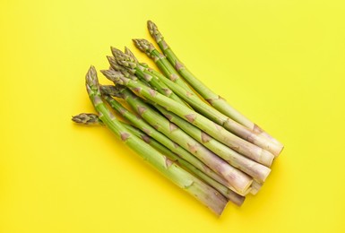 Photo of Fresh ripe raw asparagus on yellow background, top view