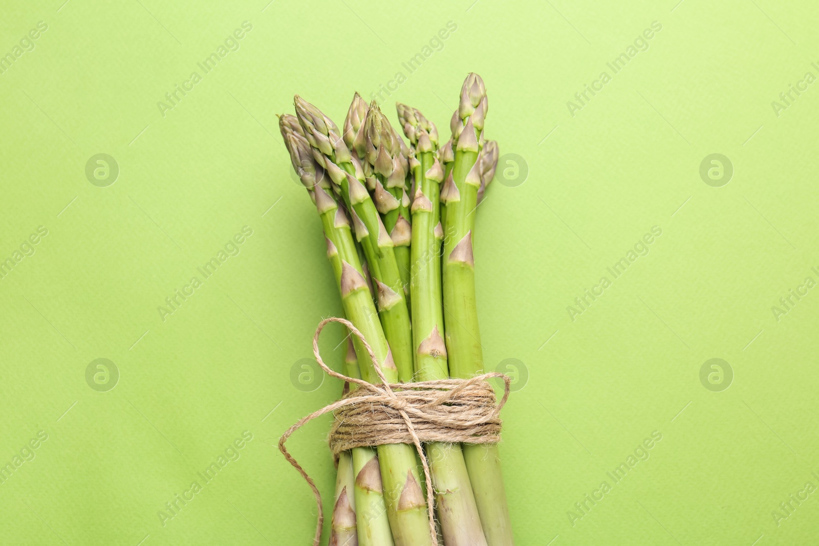 Tied raw asparagus on green background, top view Photo of Tied raw asparagus on green background, top view