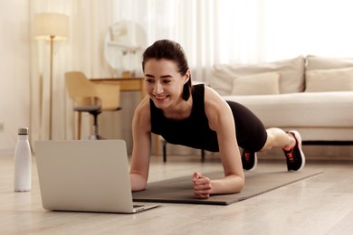 Image of Young woman doing plank exercise during online workout with coach via laptop at home. Sport and healthy lifestyle