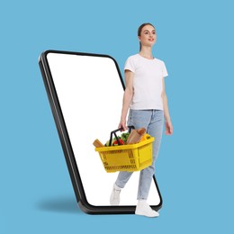 Image of Woman with shopping basket full of products walking out of mobile phone against light blue background. Online ordering