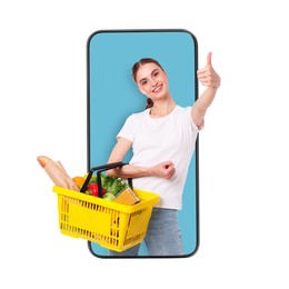 Image of Online ordering. Woman with shopping basket full of products showing thumbs-up out of mobile phone against white background