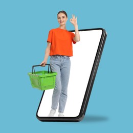 Image of Woman with shopping basket showing ok out of mobile phone against light blue background. Online ordering
