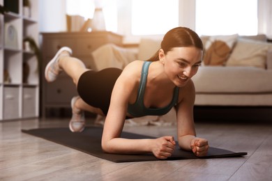 Image of Young woman doing plank exercise on fitness mat at home. Sport and healthy lifestyle