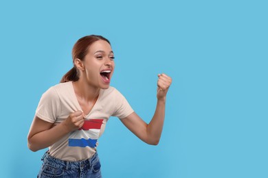 Image of Excited fan with flag of Netherlands on her t-shirt against light blue background. Space for text