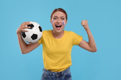 Image of Excited fan with flags of France on painted her face holding soccer ball against light blue background