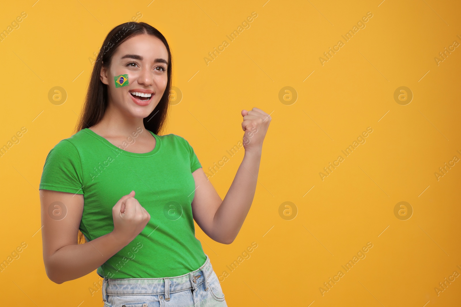 Excited fan with flag of Brazil painted on her cheek against orange background. Space for text Image of Excited fan with flag of Brazil painted on her cheek against orange background. Space for text