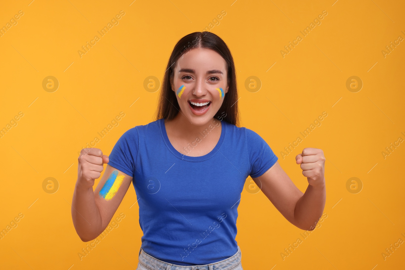 Excited fan with flags of Ukraine painted on her body against orange background Image of Excited fan with flags of Ukraine painted on her body against orange background