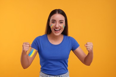 Image of Excited fan with flags of Ukraine painted on her body against orange background