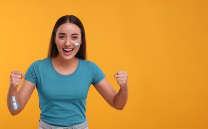 Image of Excited fan with flags of Argentina painted on her body against orange background. Banner design with space for text
