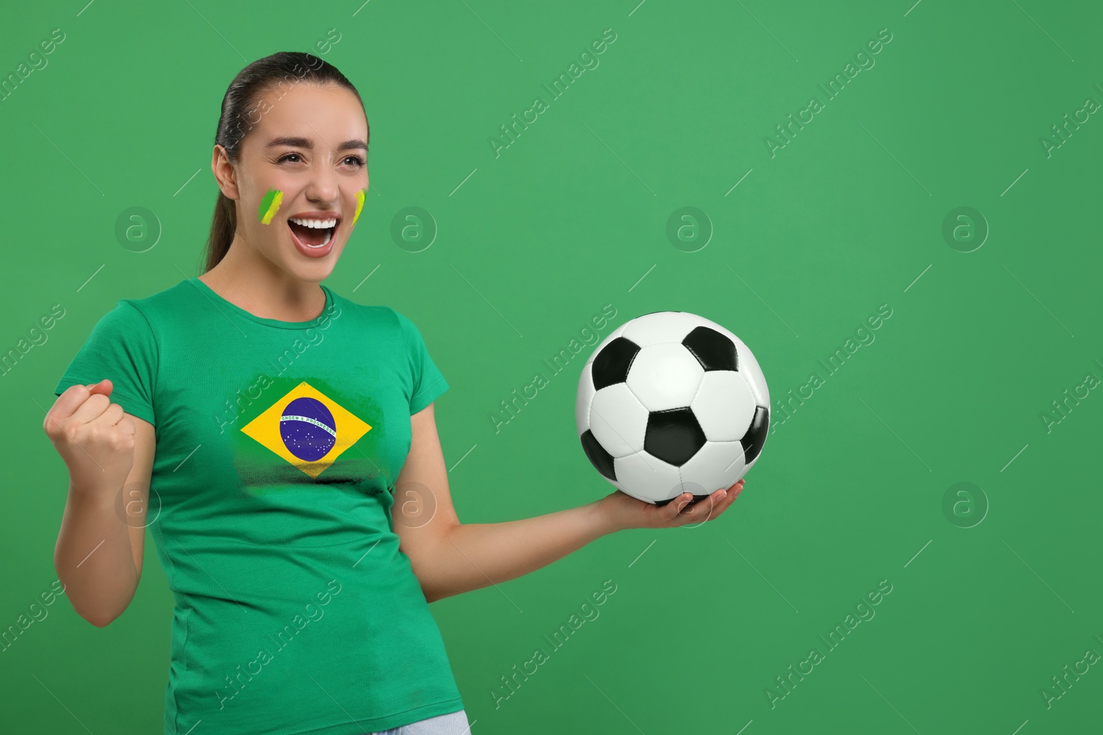 Excited fan with flag of Brazil on her t-shirt holding soccer ball against green background. Space for text Image of Excited fan with flag of Brazil on her t-shirt holding soccer ball against green background. Space for text